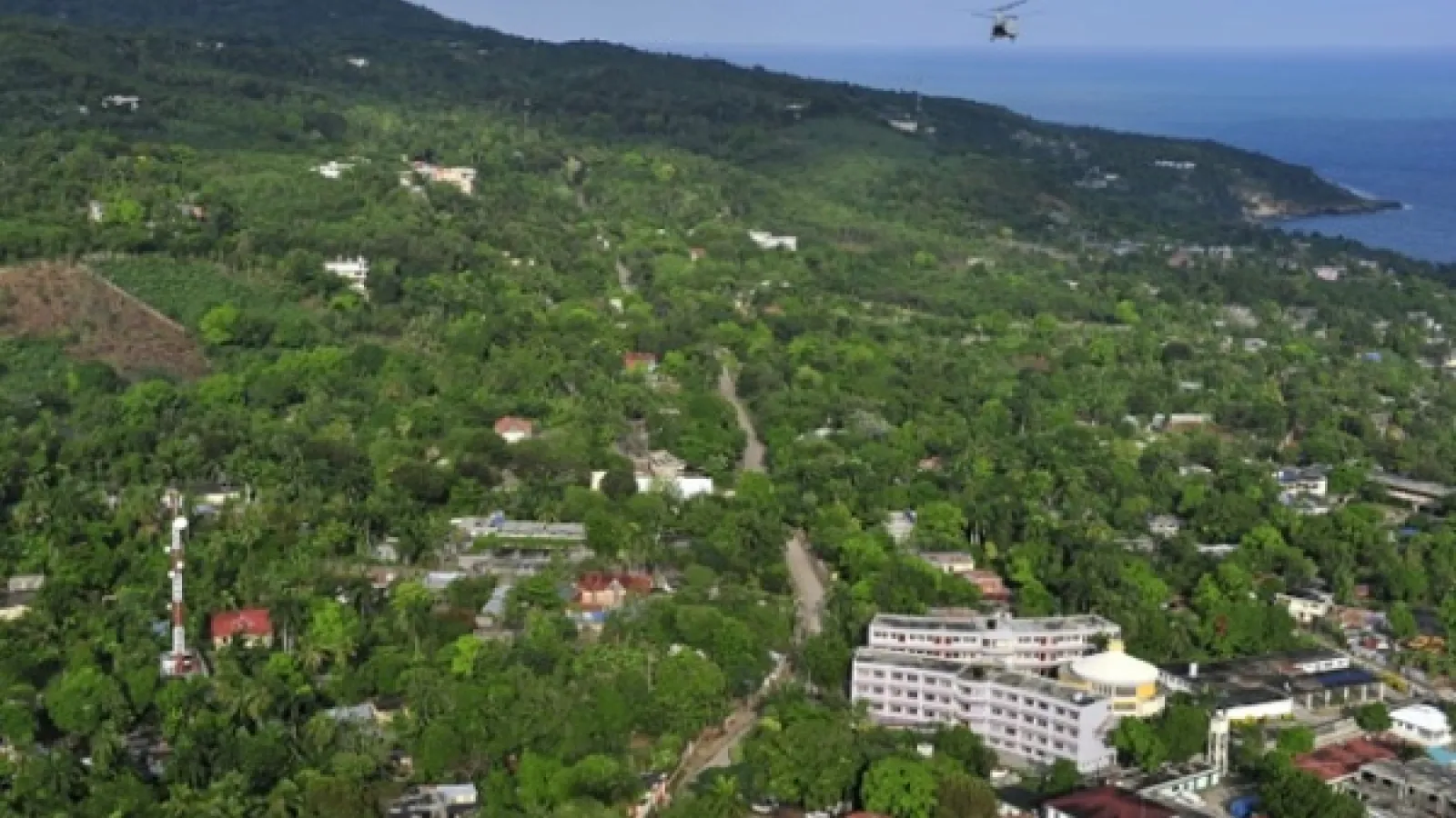 A seaside town on a hill in Haiti. A helicopter flies overhead
