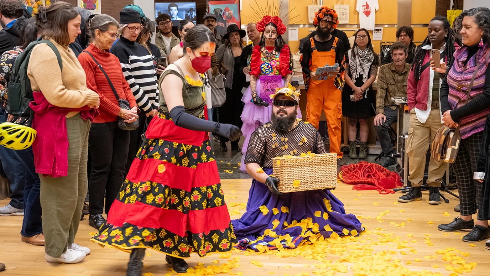 performance with marigold petals, woman standing, man with beard sitting and holding basket