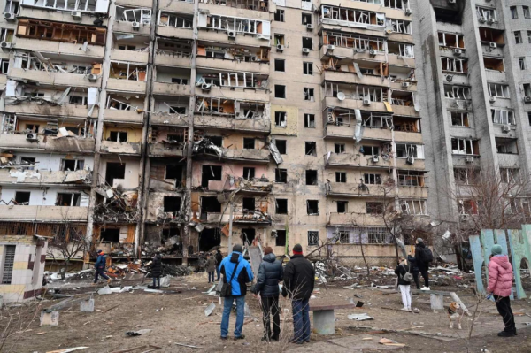 People look at a damaged residential building at Koshytsa Street, a suburb of the Ukrainian capital, Kyiv, where an artillery shell hit, on Feb. 25. GENYA SAVILOV/AFP