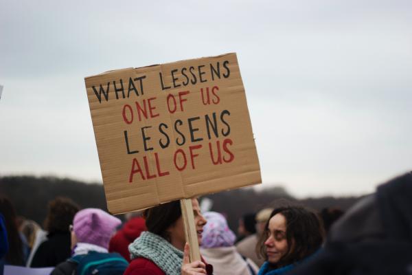 Protest sign that says "What lessens one of us lessens all of us"