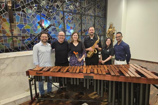 People standing behind a Marimba with a mosaic on the background