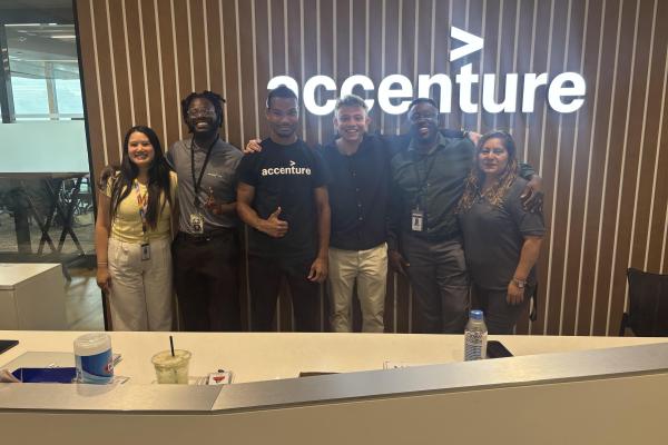 group of 6 people next to each other in front of sign that says Accenture