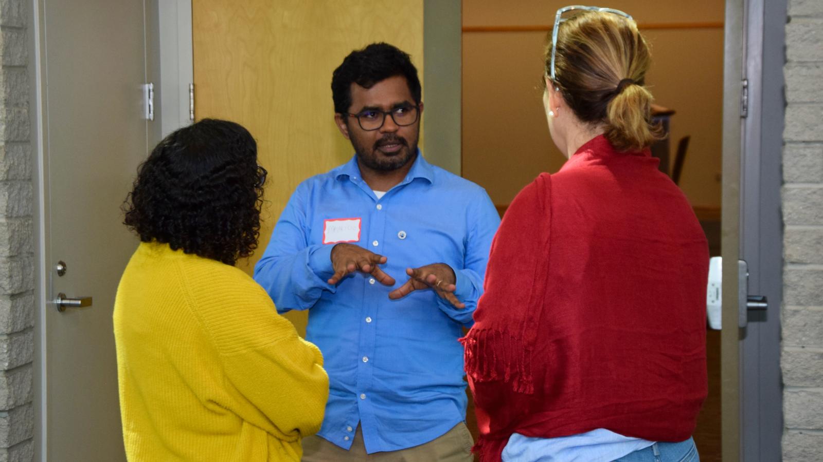 man in blue talking with two women (wearing green and red)