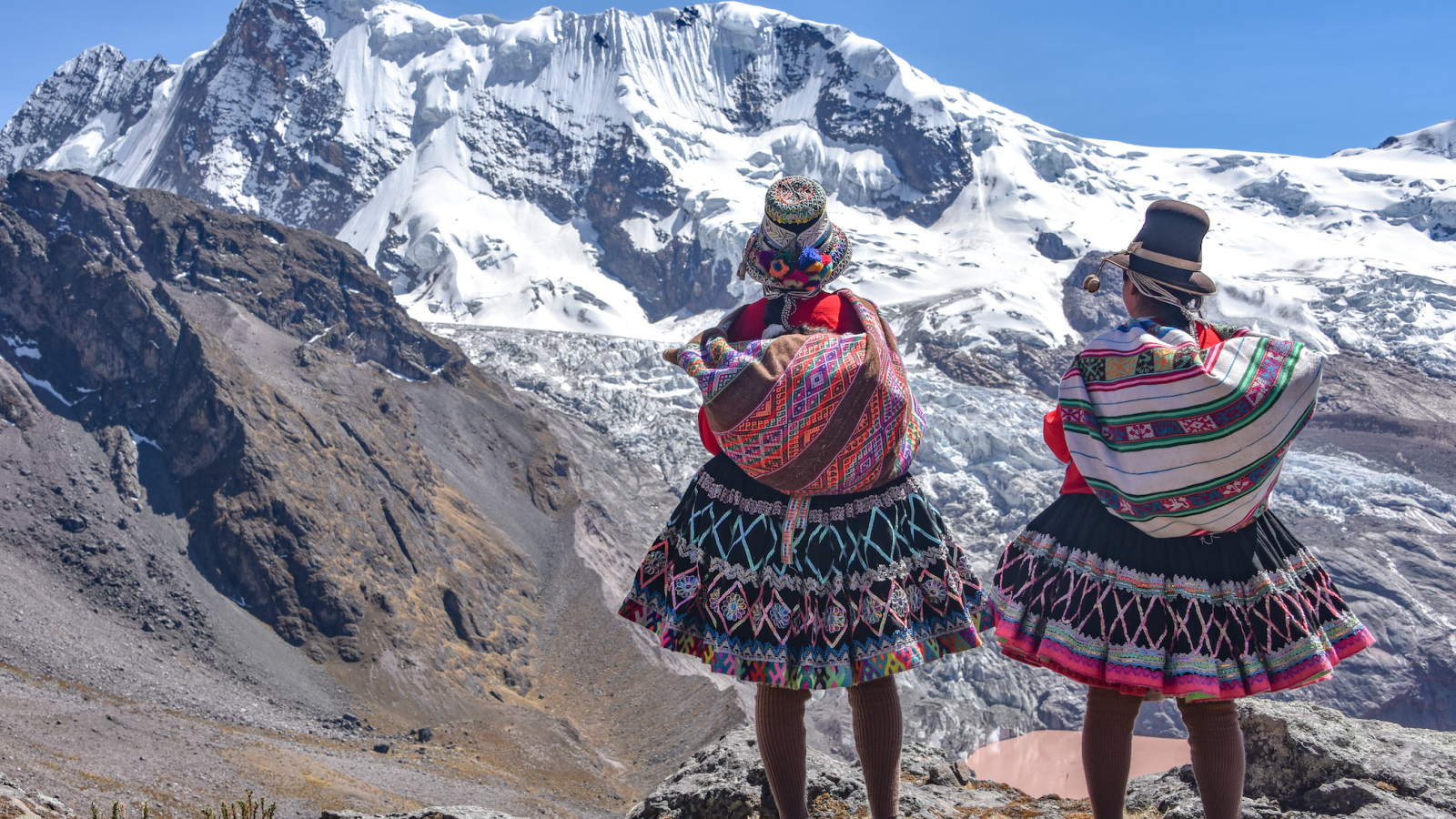 back of two indigenous Latin American women facing snowy mountain